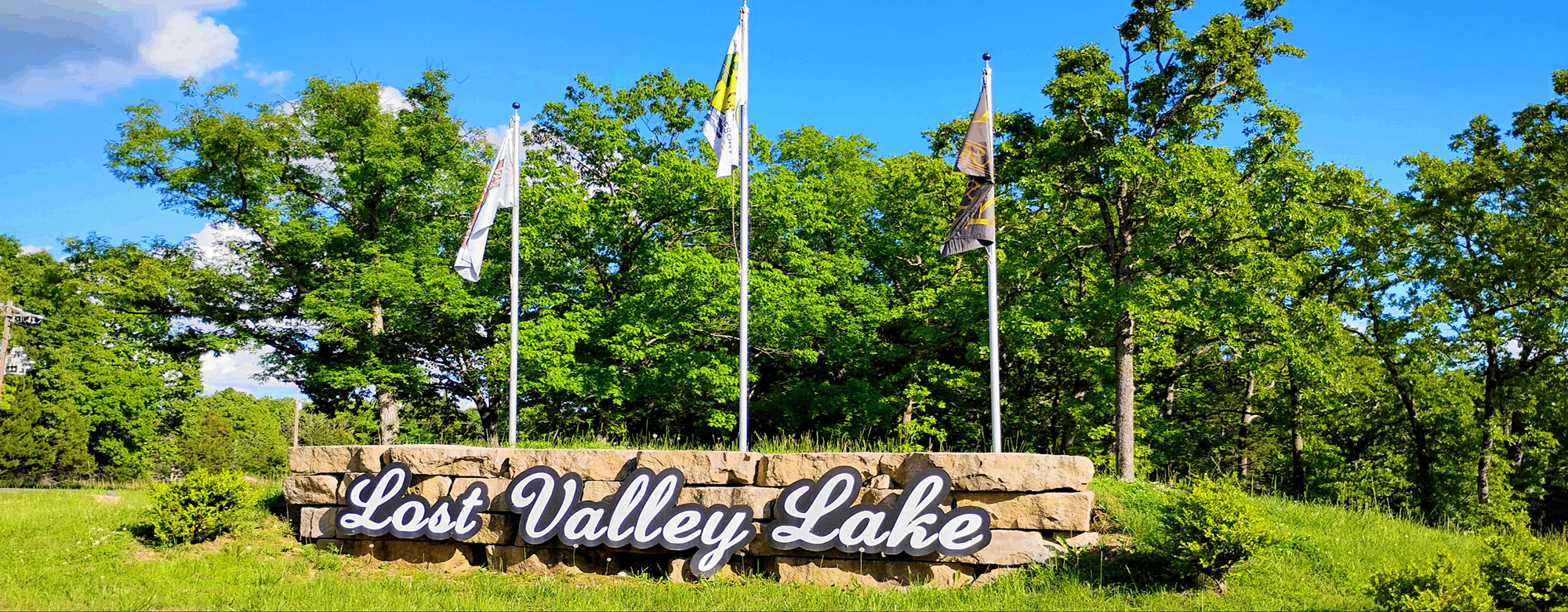 Lost valley lake sign with three flags and trees behind it.