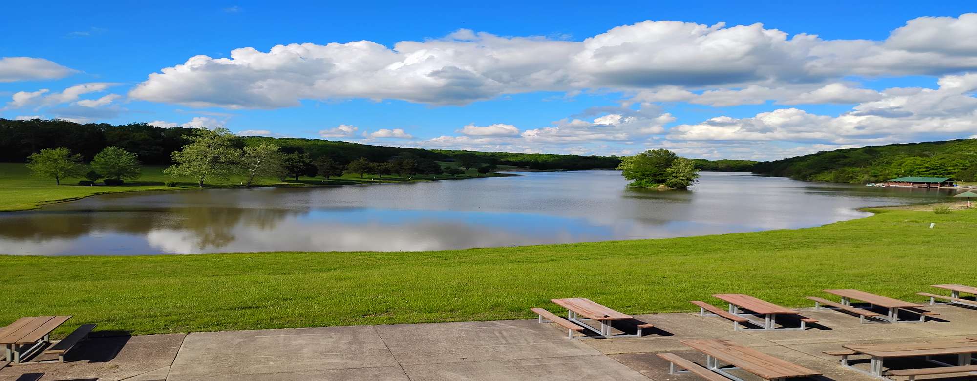 image of a lake in summer with green grass and a pattio