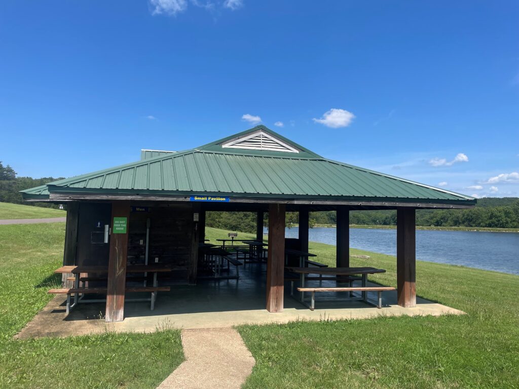 small pavilion with a green roof and wooden beams.